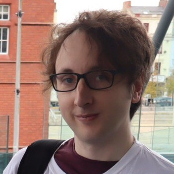 A photo of Ben, who is in their thirties with medium-length hair and wearing black-rimmed glasses